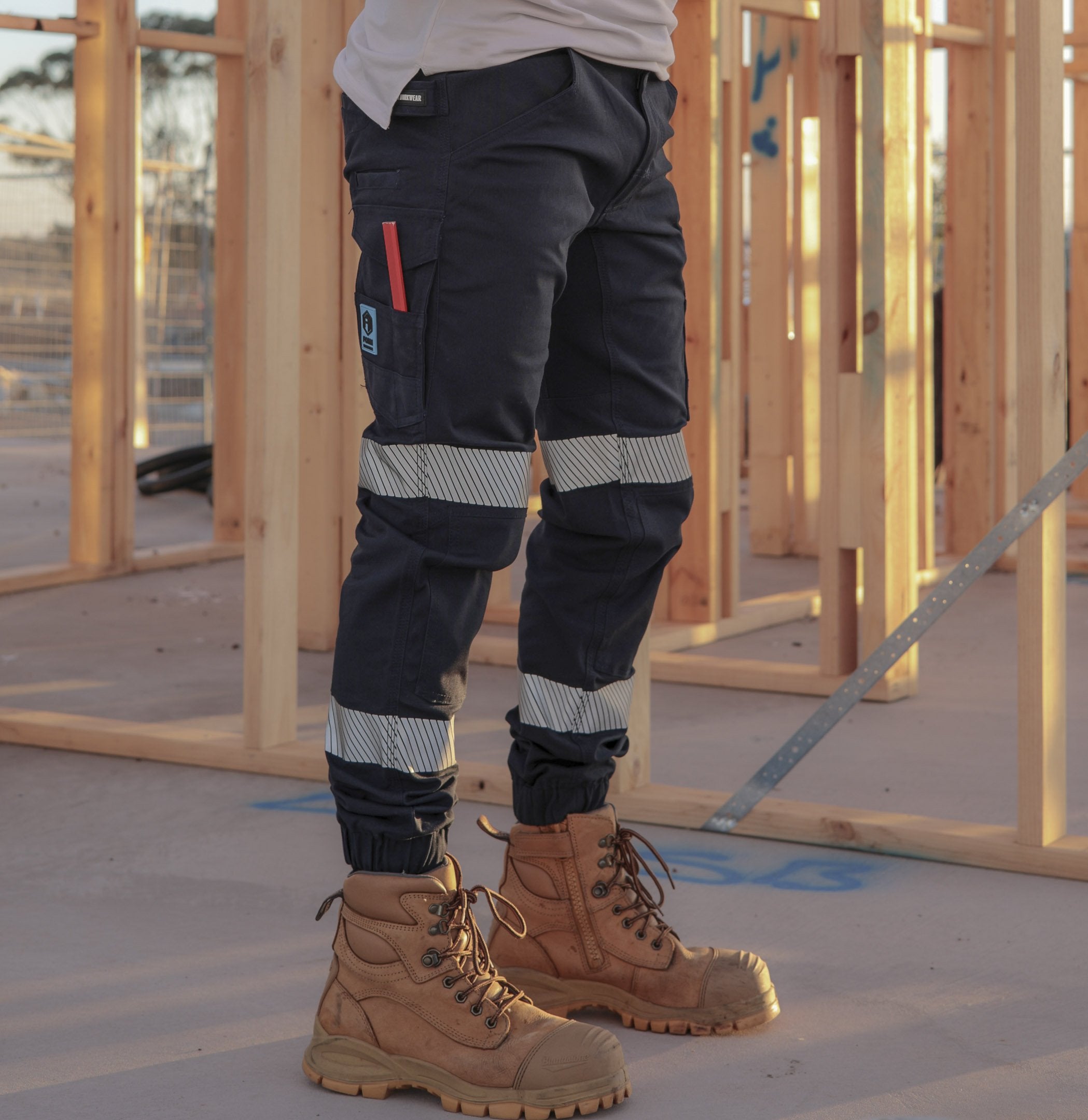 Tradie wearing FB1 navy hi-vis cuffed work pants with reflective tape on construction site