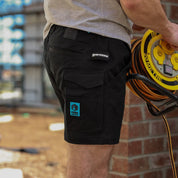 Tradesman wearing Form Workwear black cargo shorts holding an extension cord reel at a construction site