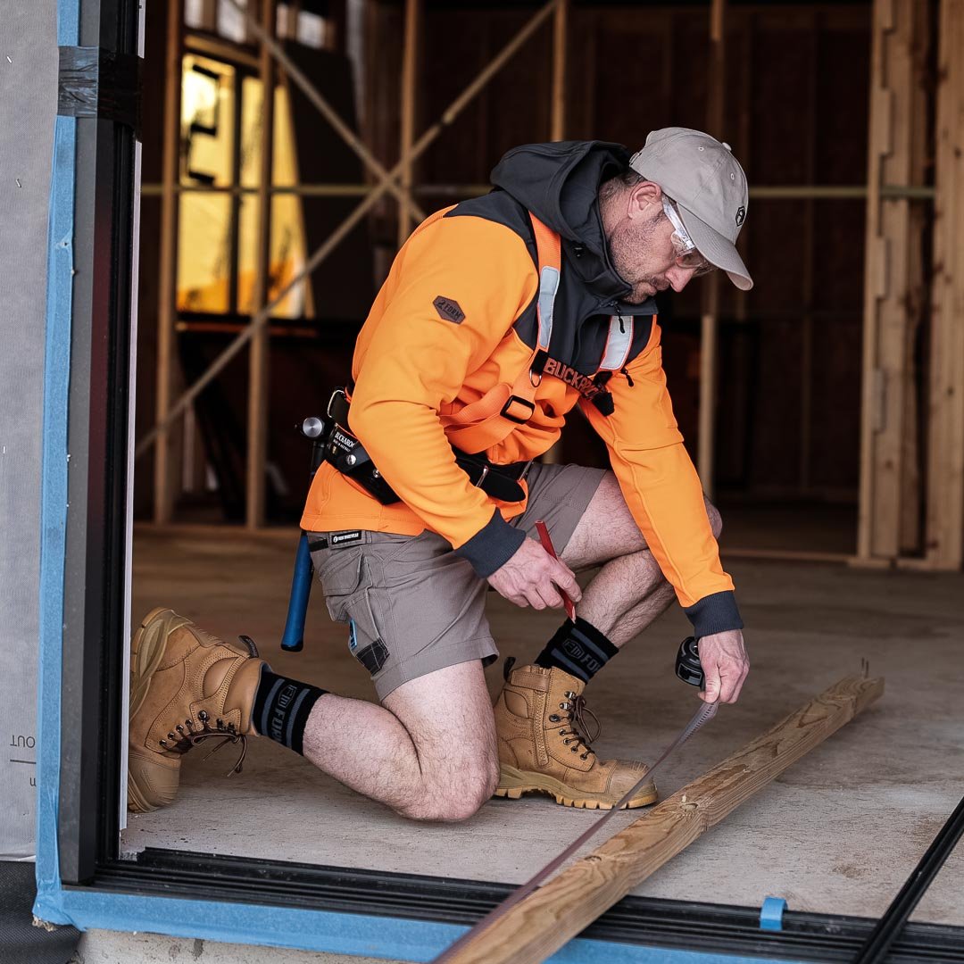 Tradesman in hi-vis orange Form Workwear hoodie kneeling and marking a wooden board on site