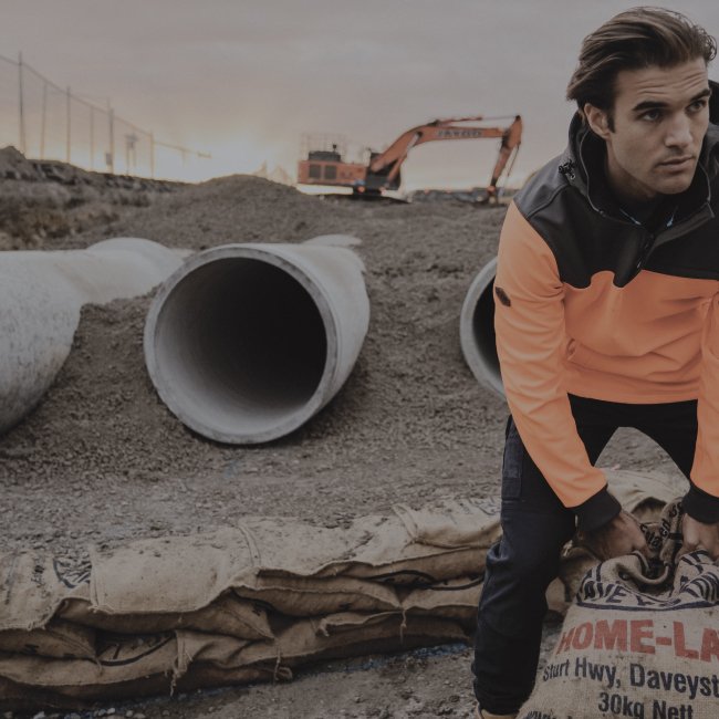 construction worker wearing hi vis orange hoody on a construction site with drainage pipes and orange excavator