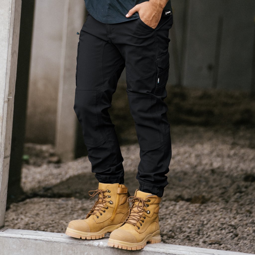 Black work pants for tradesmen paired with tan safety boots, ideal for construction and outdoor jobs