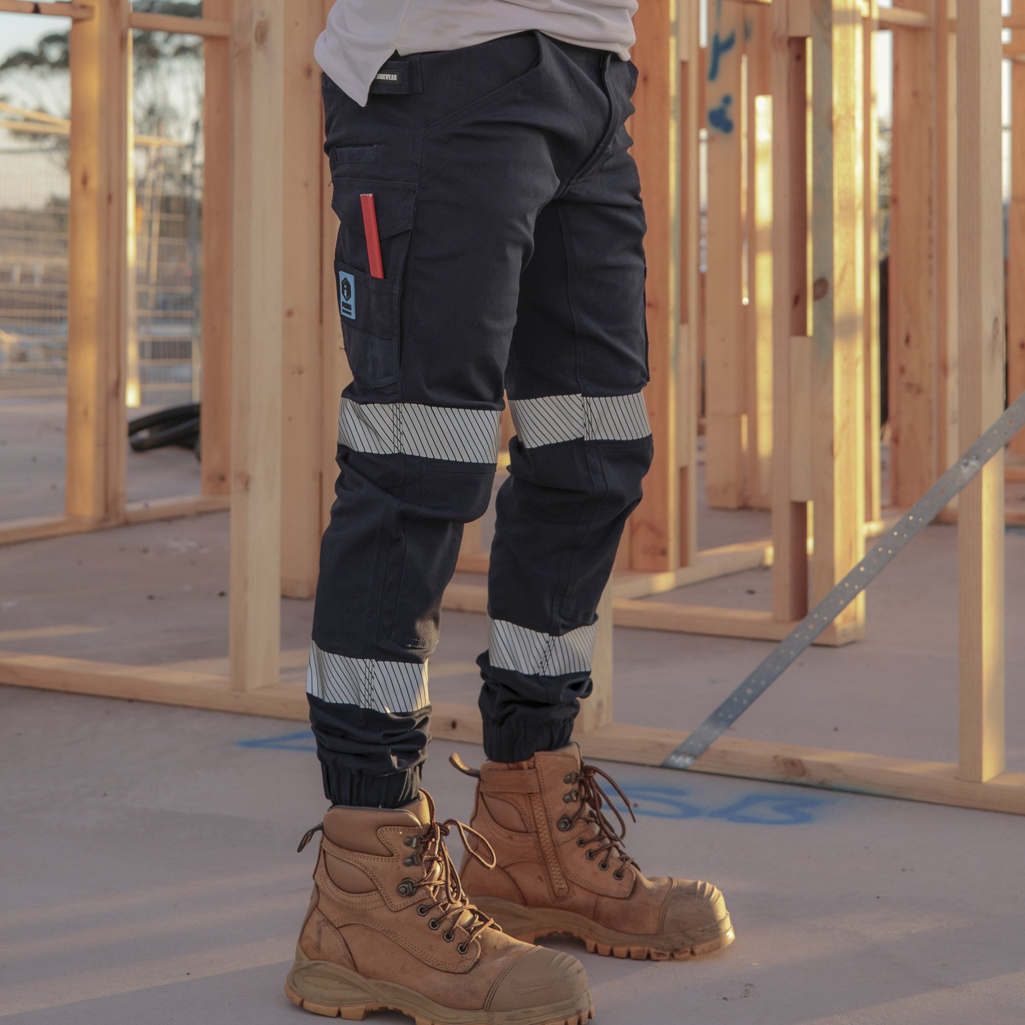 Tradie wearing FB1 navy hi-vis cuffed work pants with reflective tape on construction site