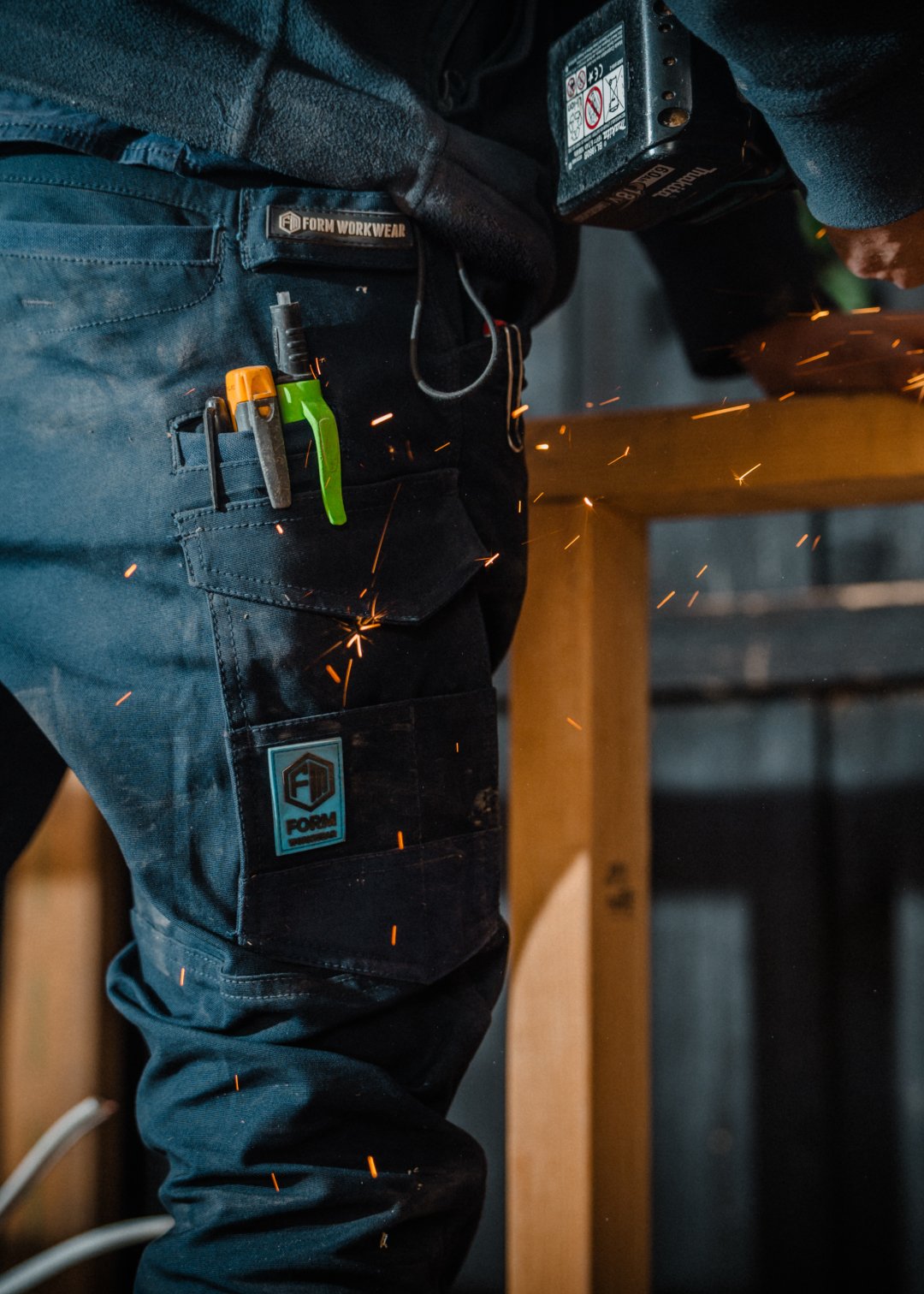 Close-up of FB1 navy work pants with tools in pocket and sparks flying on job site