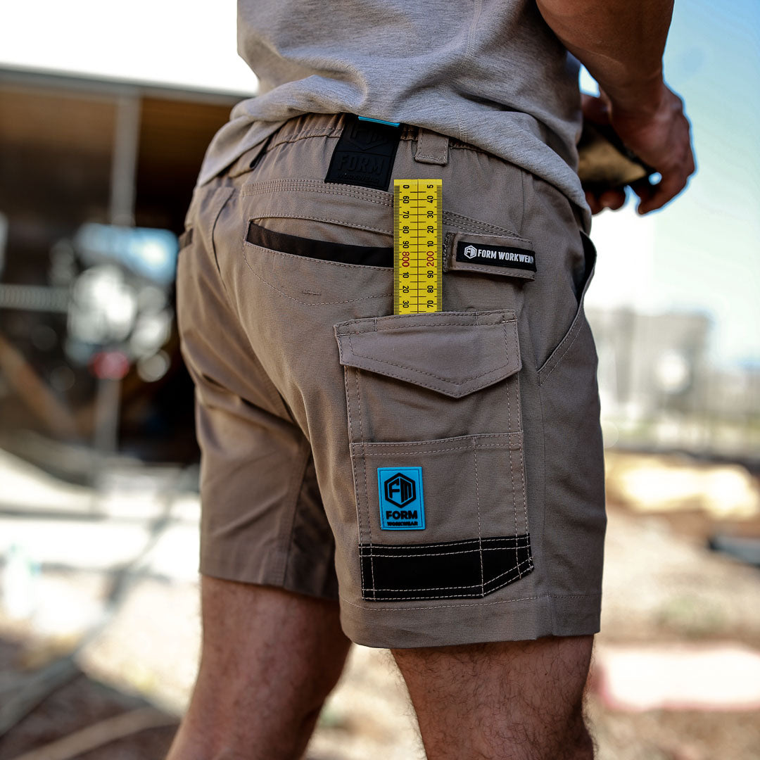 Tradesman wearing Form Workwear khaki cargo shorts with a measuring tape in the pocket, working at a construction site