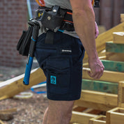 Tradesman wearing Form Workwear navy cargo shorts with a tool belt and hammer at a construction site.
