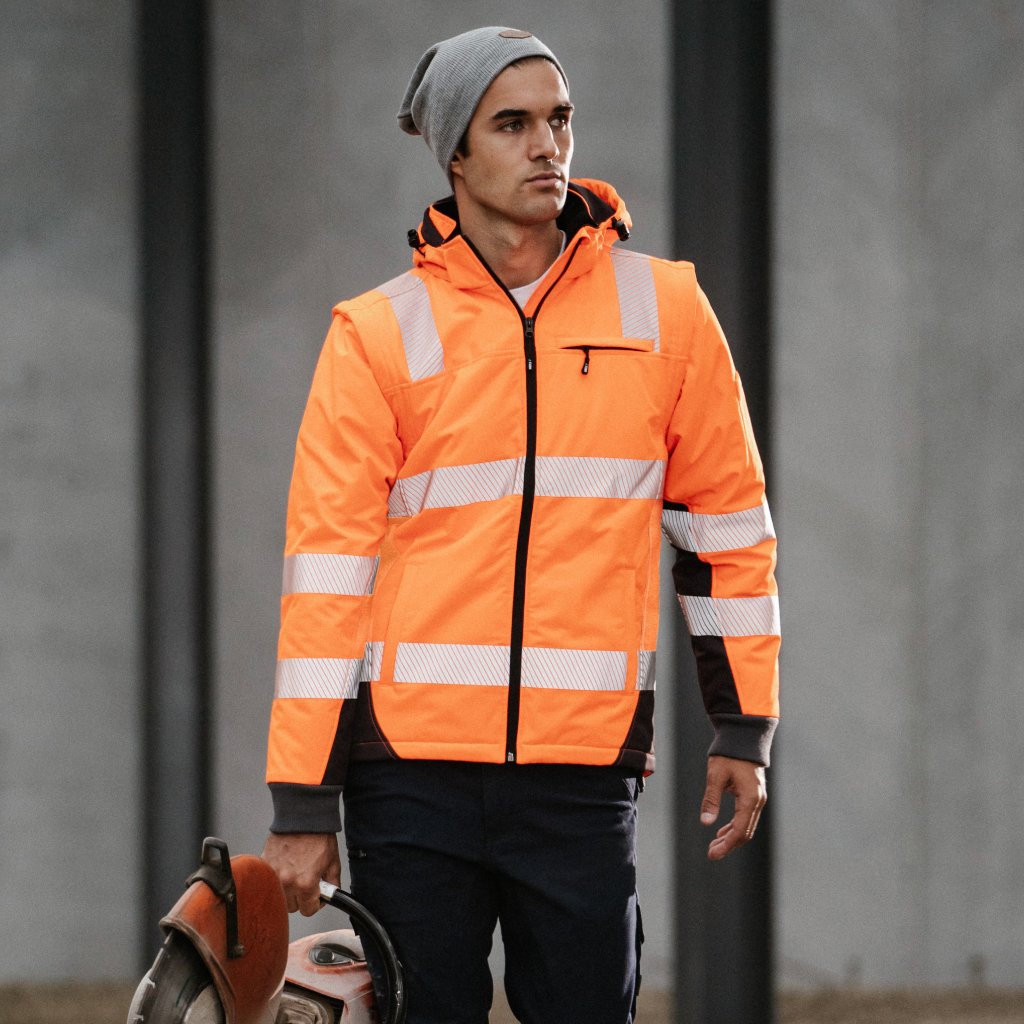 Tradesman wearing hi-vis orange Form Workwear jacket holding a chainsaw