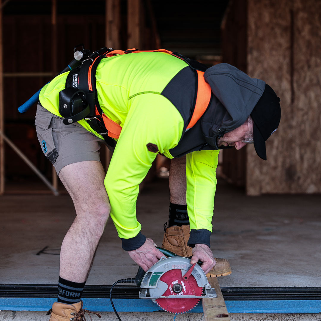 Tradesman wearing hi-vis yellow hoodie cutting wood on construction site