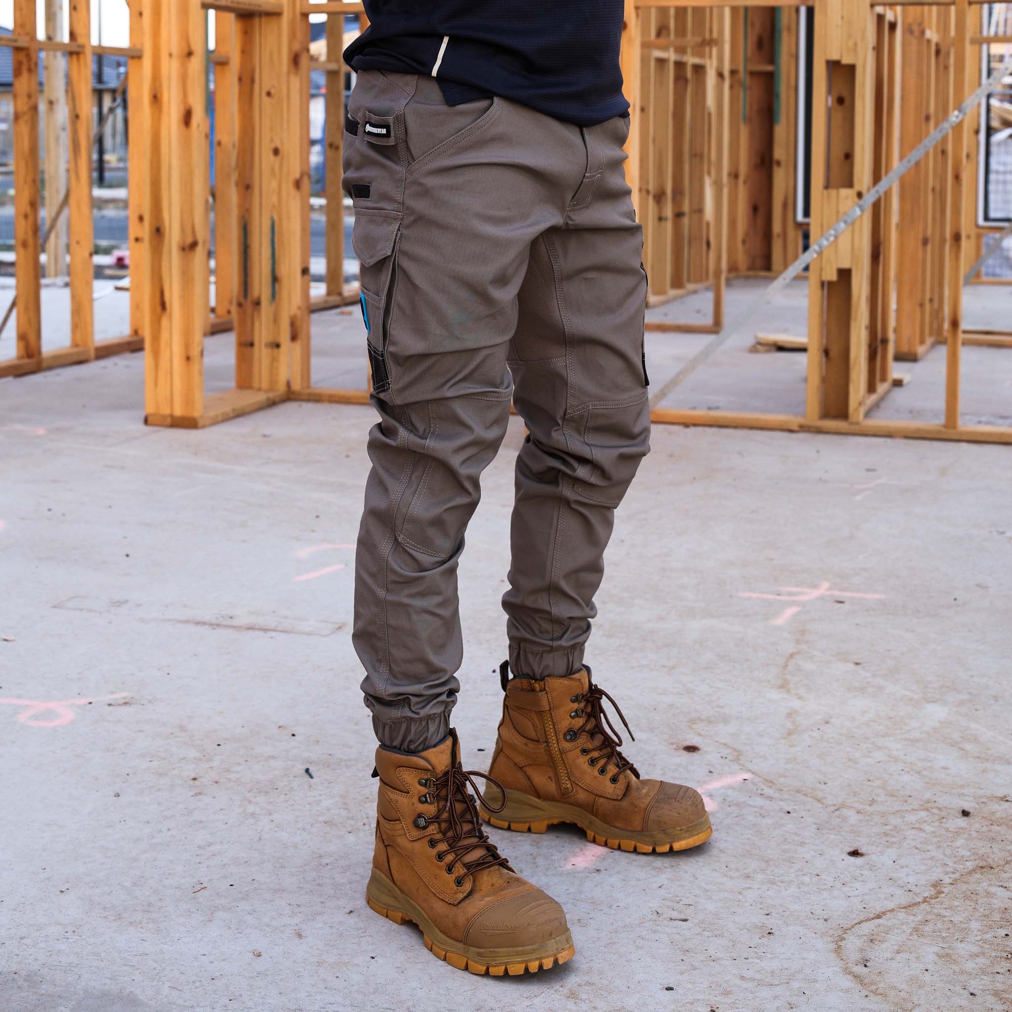 Tradesman wearing Form Workwear khaki cargo pants and tan work boots at a timber frame construction site