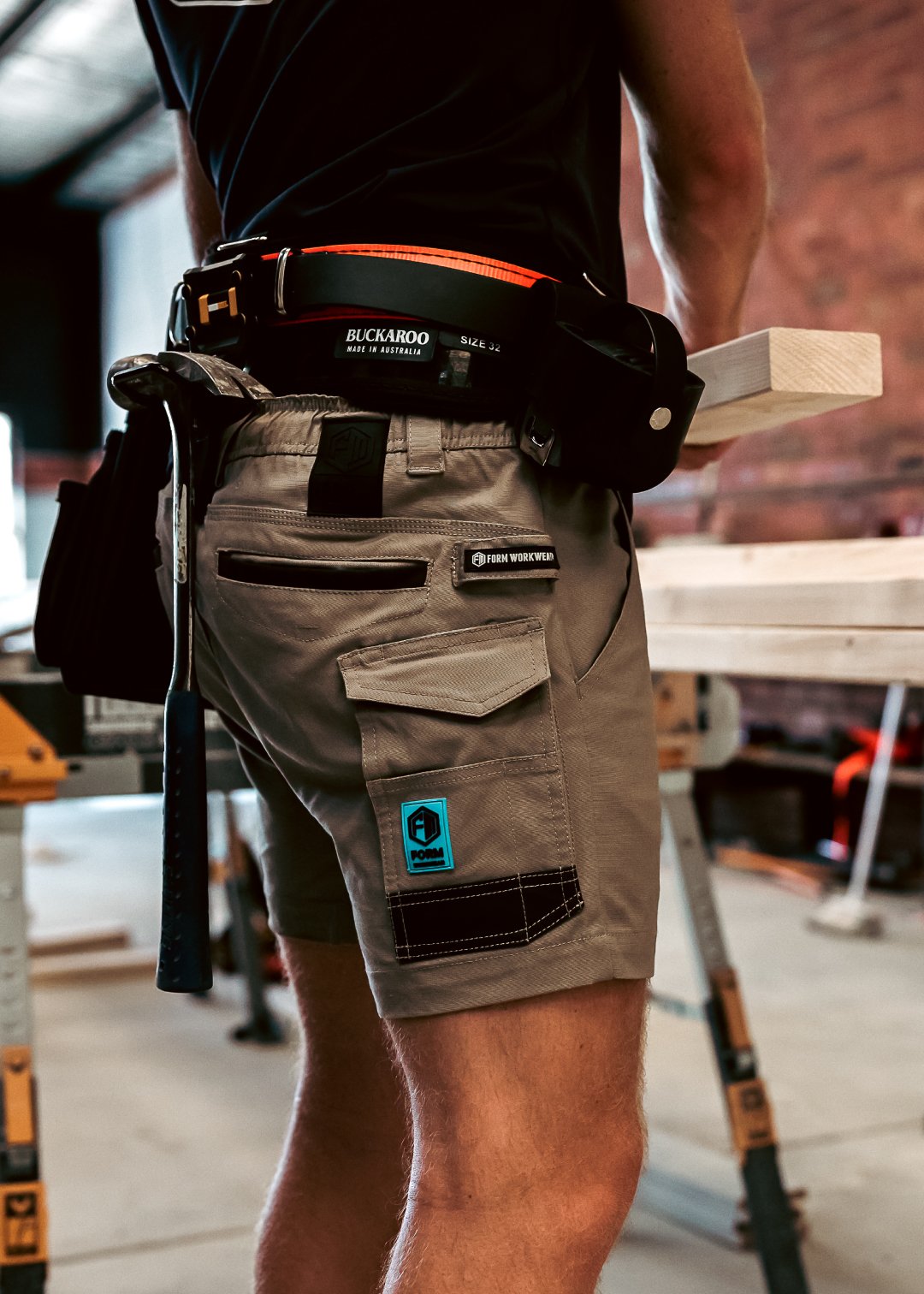 Tradie wearing Form Workwear khaki utility shorts with tool belt in workshop setting