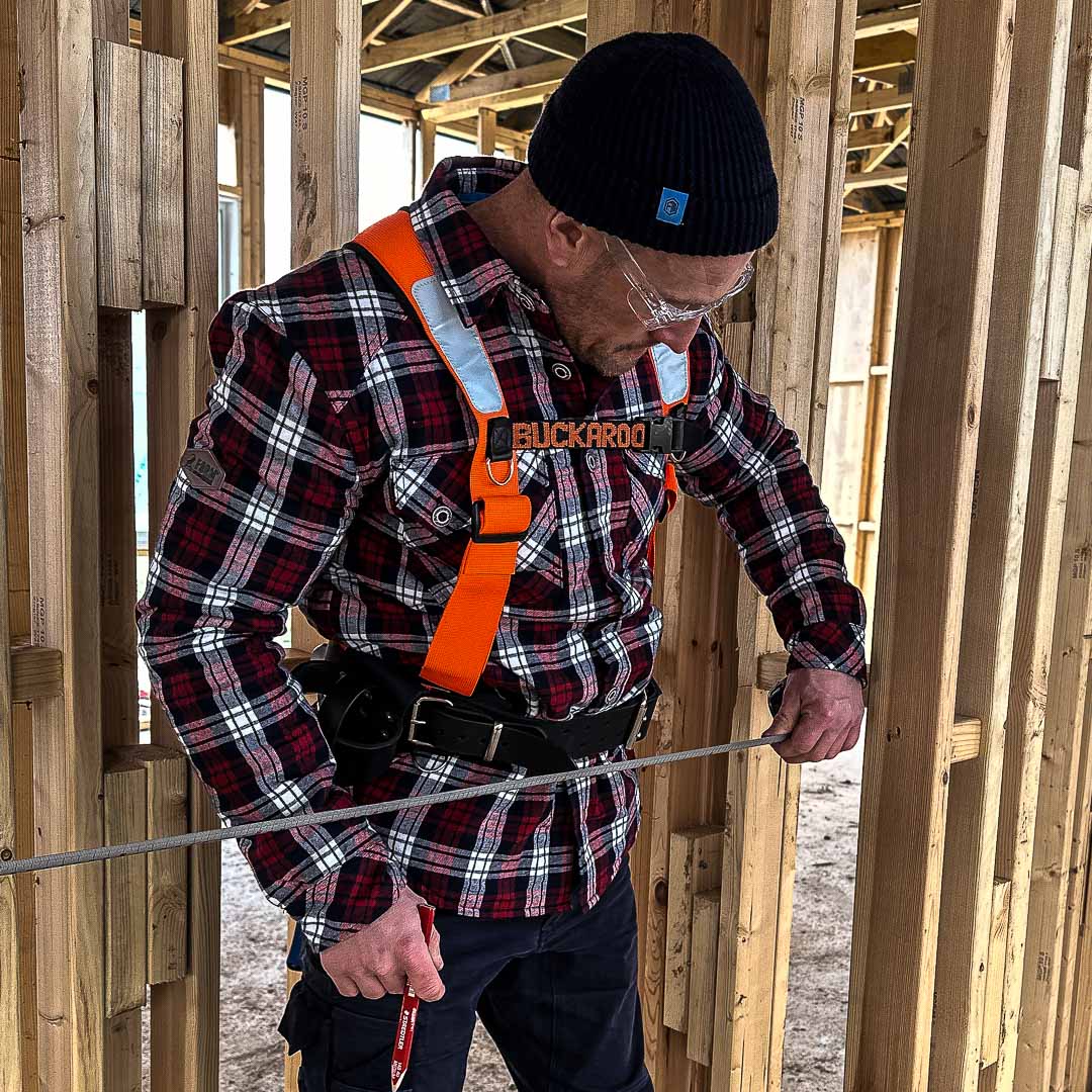 Tradesman in a red plaid shirt wearing a Buckaroo safety harness while working on a construction site